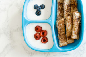 A blue kid's plate filled with strips of french toast and yogurt with berries