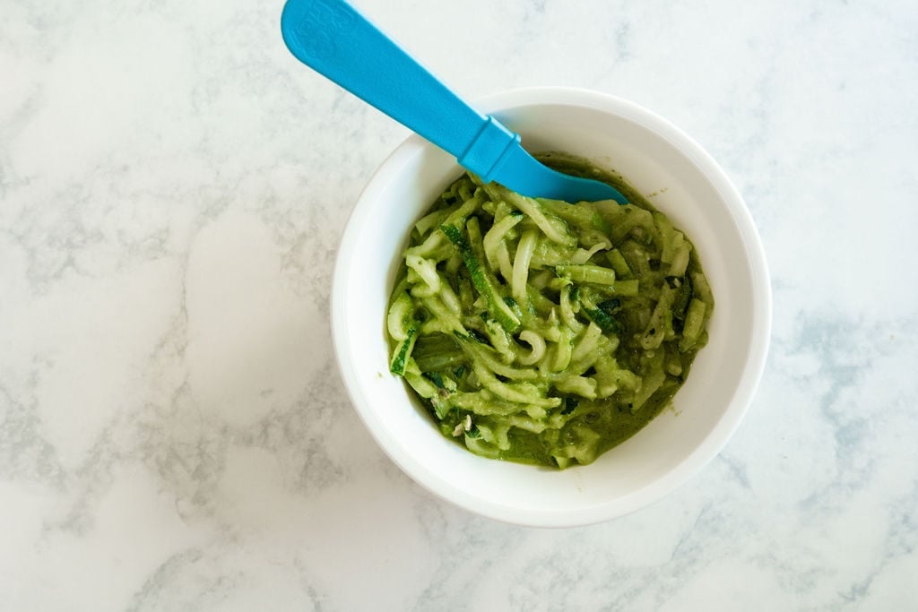 White bowl filled with zoodles and pesto and a blue fork sticking out