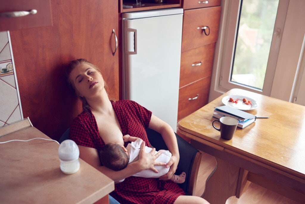 sleepy and exhausted mother trying to breastfeed her baby girl, photo taken indoors.