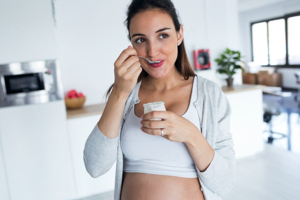 Shot of beautiful pregnant young woman eating yogurt at home.