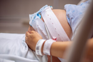 Childbirth and labor. A pregnant woman in the hospital having contractions and tests. External monitors are wrapped around her pregnant belly to monitor her contractions and her baby's heart rate.