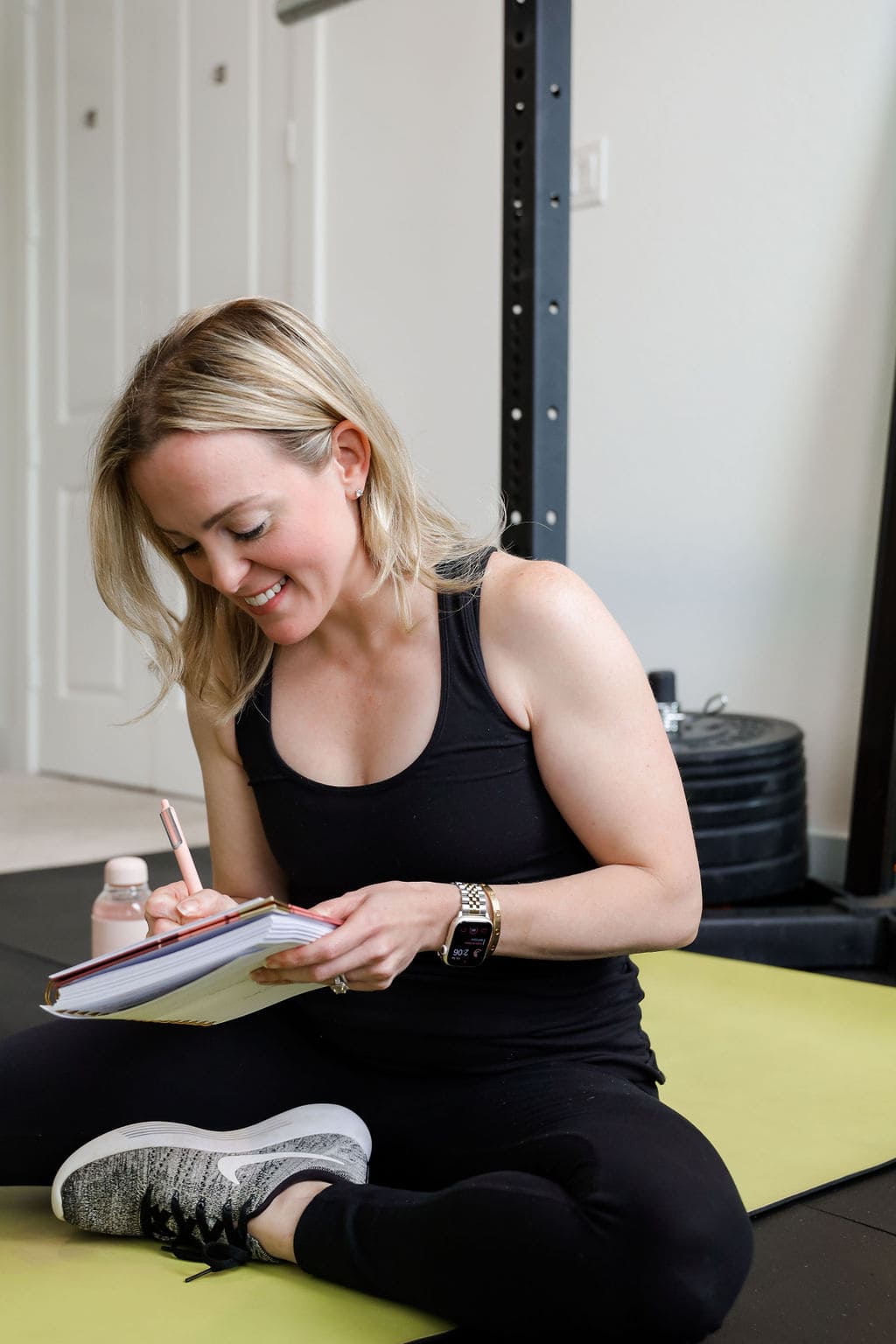 Nina Spears sitting on the floor in a gym wearing athletic apparel writing in her motherhood planner.