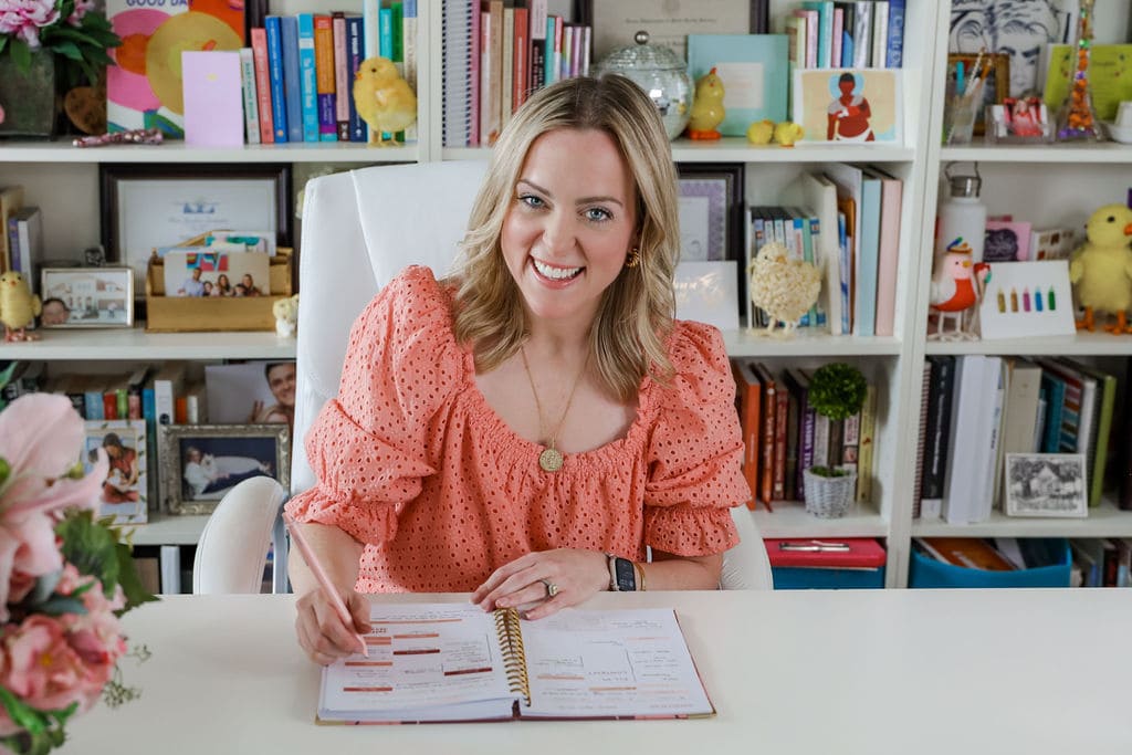 Nina Spears, The Baby Chick, sitting at her desk in her office writing inside of her motherhood planner.