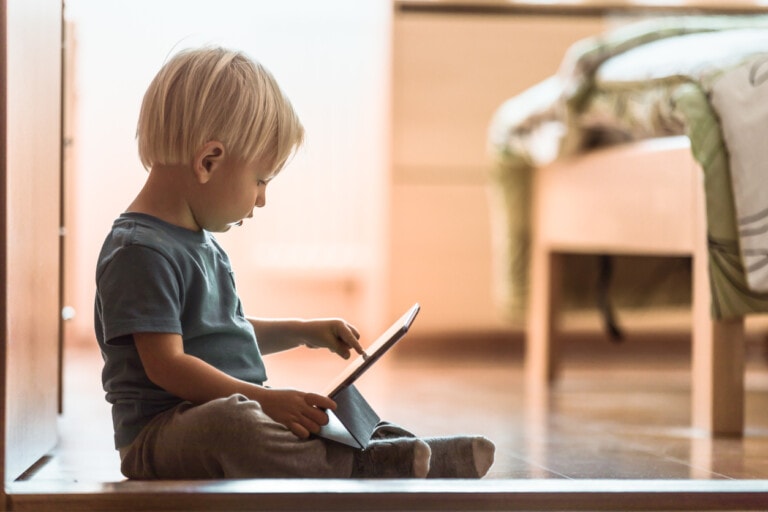 Toddler boy sitting on the floor looking at a smart tablet.