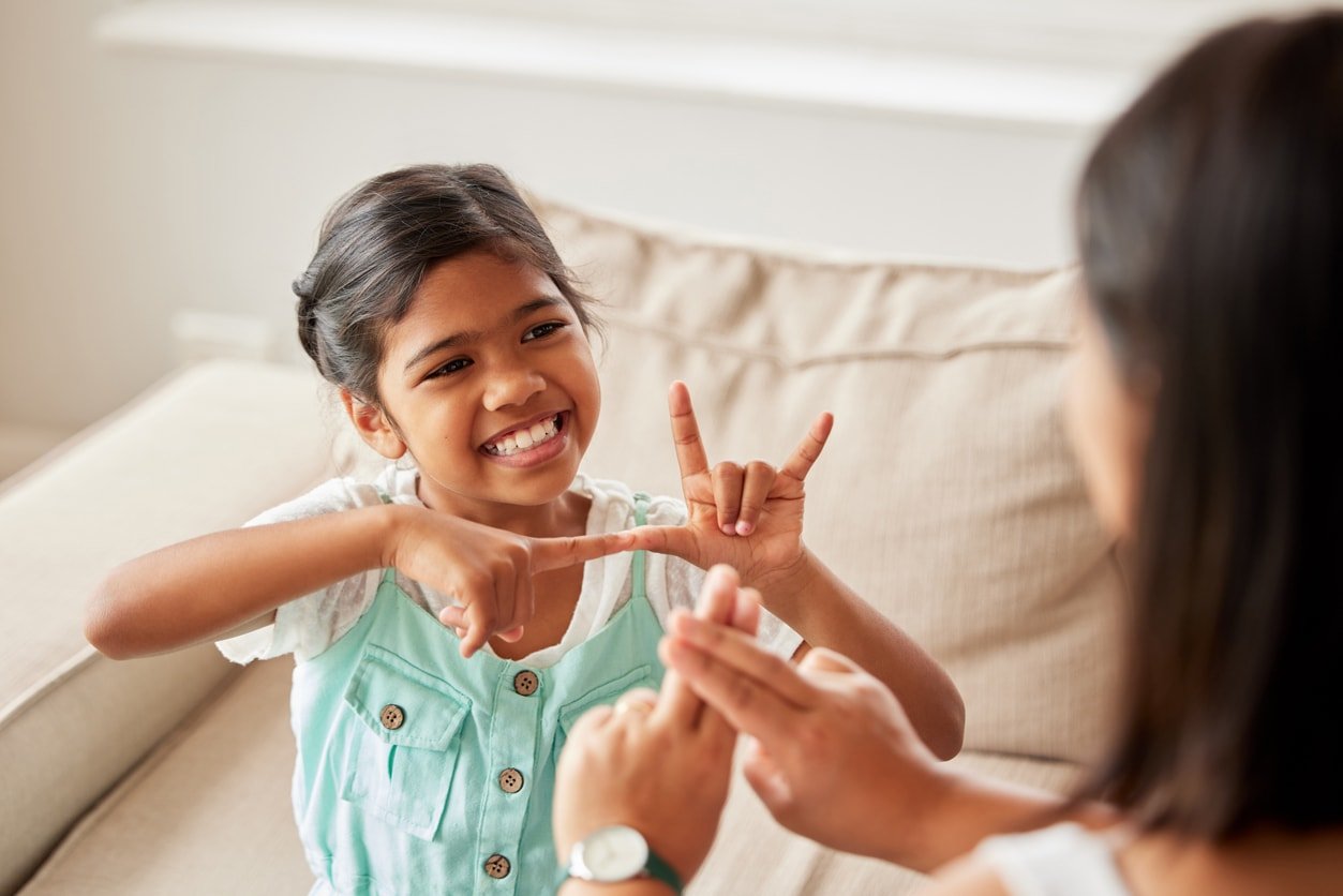 Little girl counting and learning basic sign language while being homeschooled by her mother on the sofa