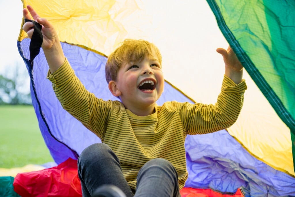 Young boy at preschool playing with a parachute in the North East of England.