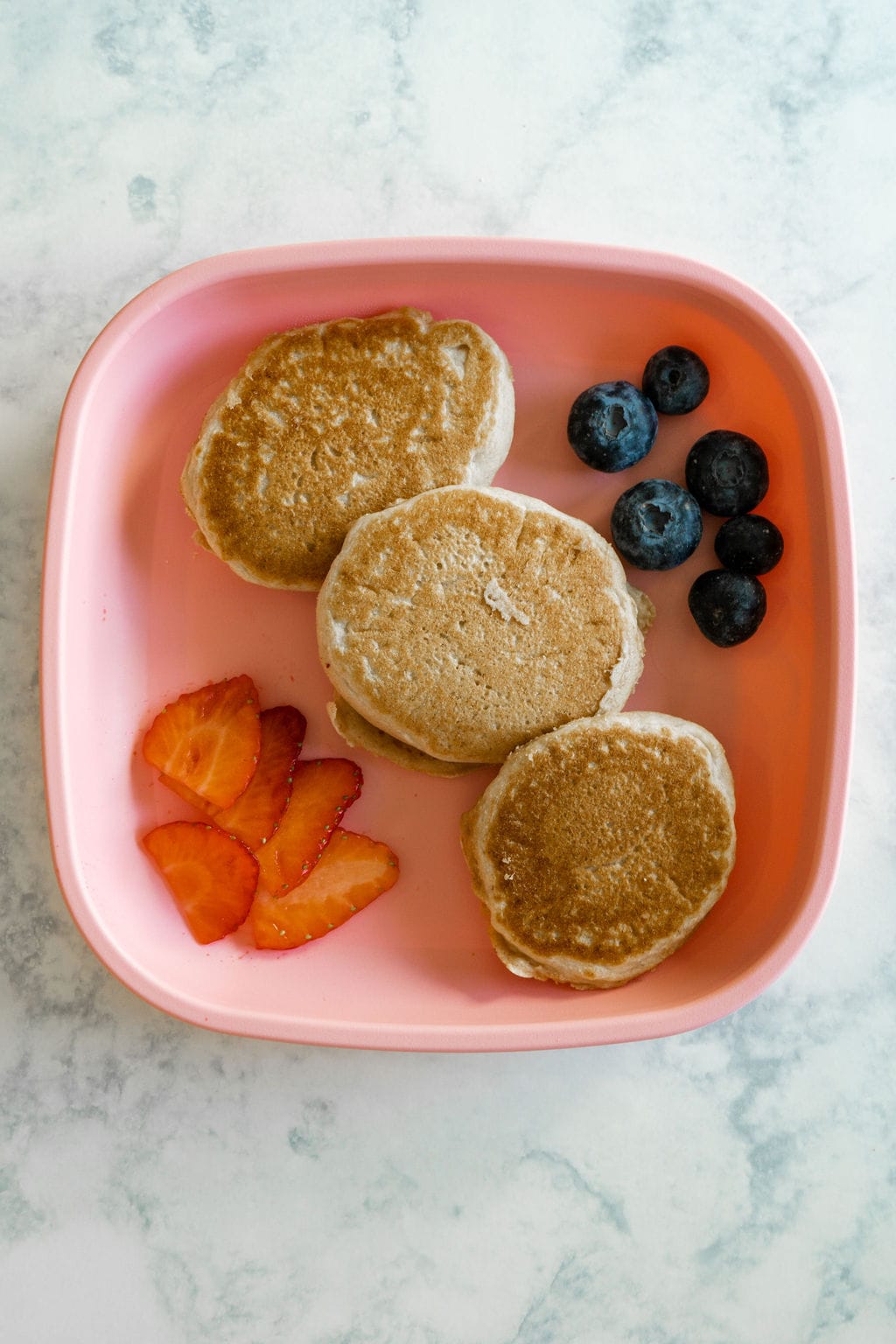 Pink kid's plate with pancakes and fruit.