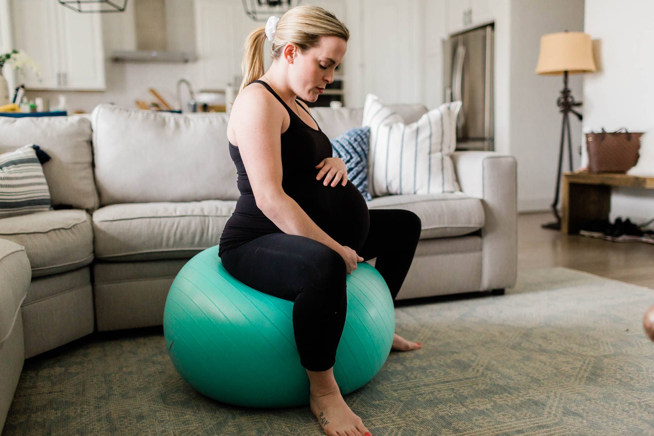 Pregnant woman sitting on a birthing ball in her living room.