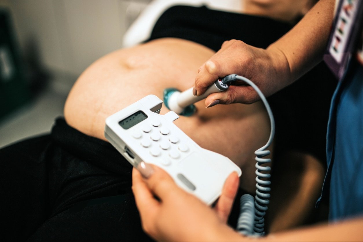 Pregnant woman lying down and a midwife is using a doppler to listen to baby's heart beat on the pregnant woman's belly.
