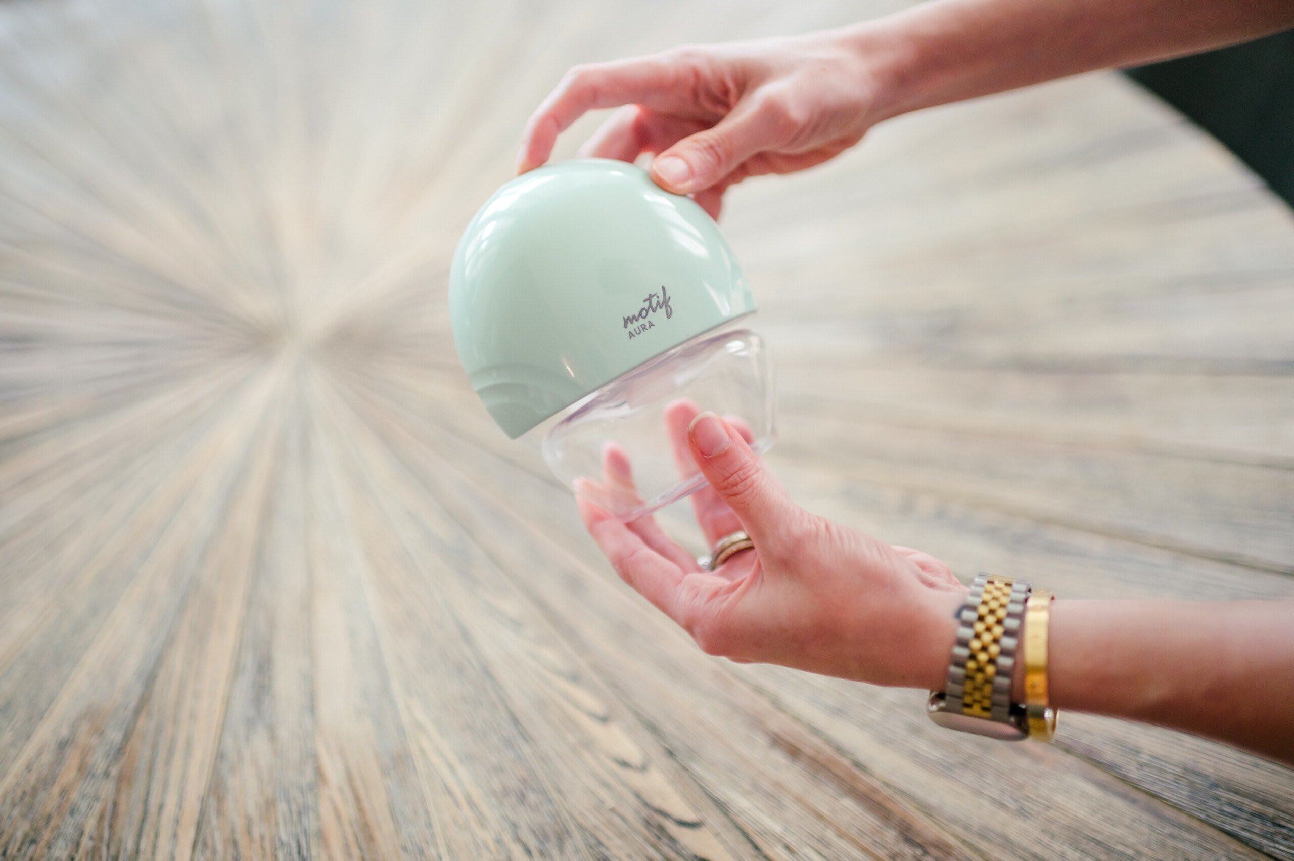 Hands holding one of the Motif Aura breast pumps