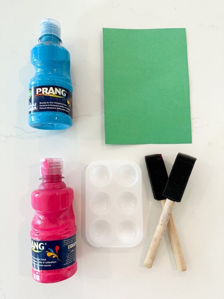 Kids paint, construction paper, a painter's palette and paint brushes on a white counter