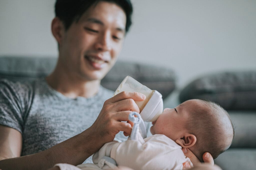 Asian Chinese young father feeding his baby boy son with milk bottle at living room during weekend