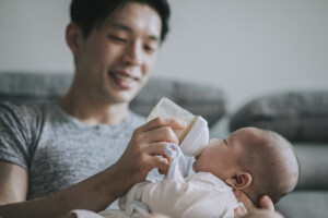 Asian Chinese young father feeding his baby boy son with milk bottle at living room during weekend