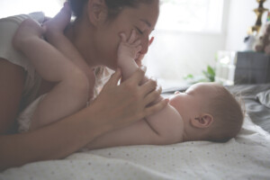 Mother playing with her baby on the bed holding and kissing baby's hands.