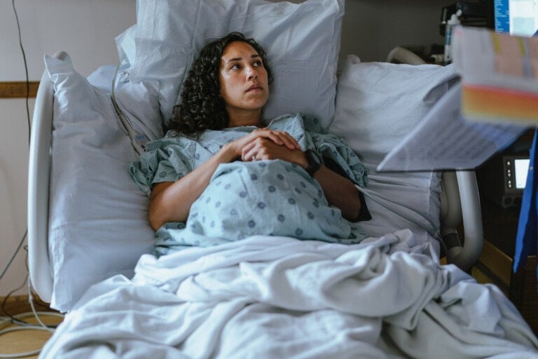 A pregnant multiracial woman of Hawaiian descent lies in a hospital bed and speaks with her doctor while in labor.