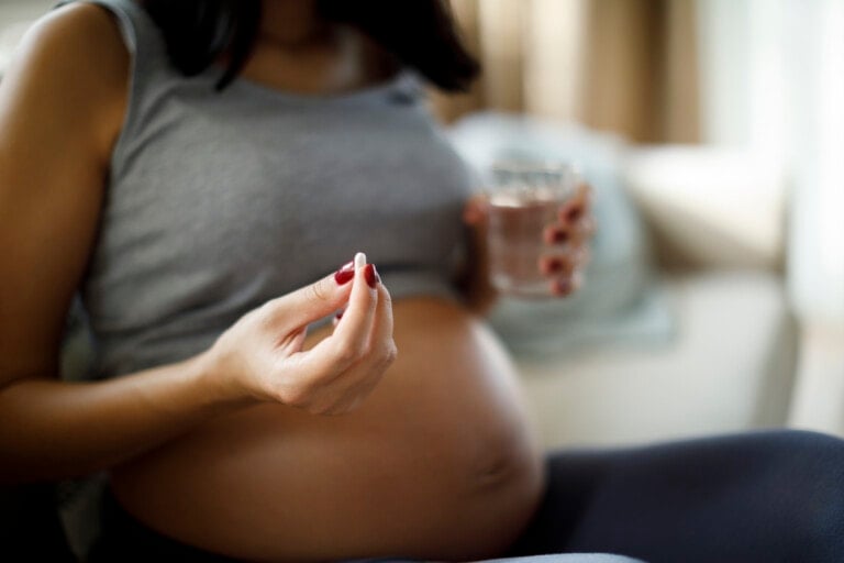 Pregnant woman taking pill at home and holding a glass of water