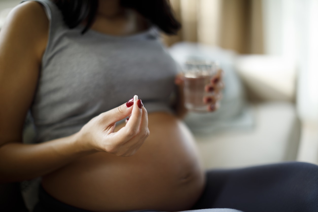 Pregnant woman taking pill at home and holding a glass of water