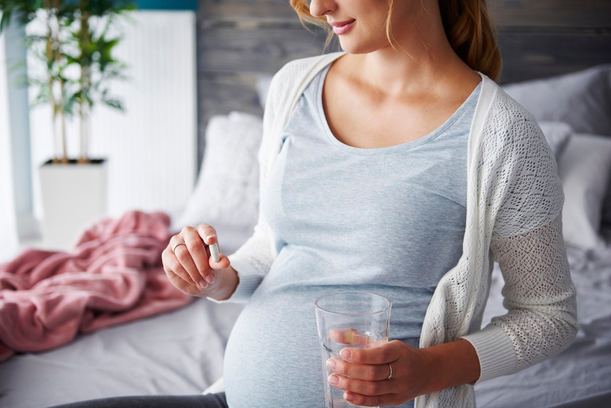 Young pregnant woman taking capsule and holding a glass of water