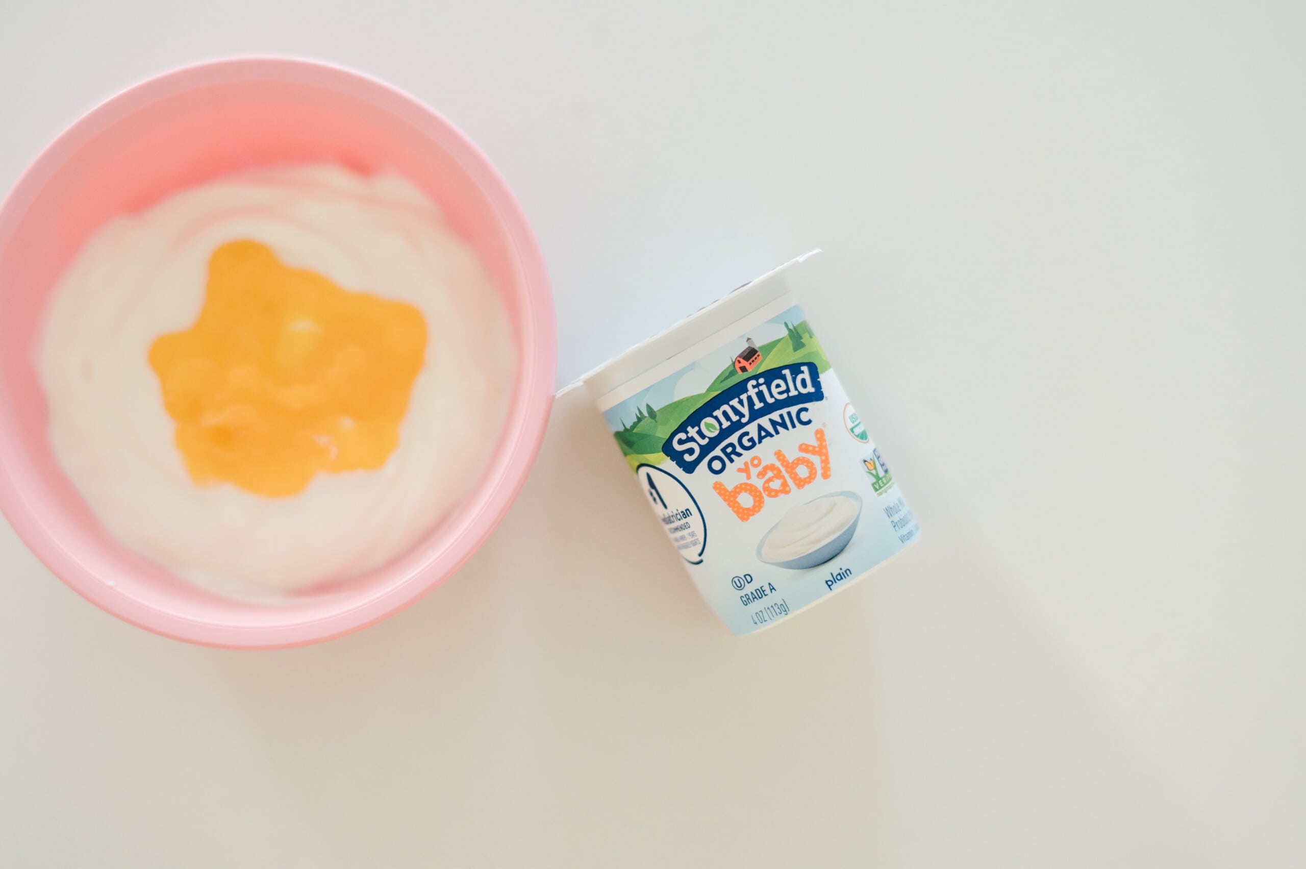 Bowl of yogurt and mashed peaches with a cup of Stonyfield Yobaby plain yogurt