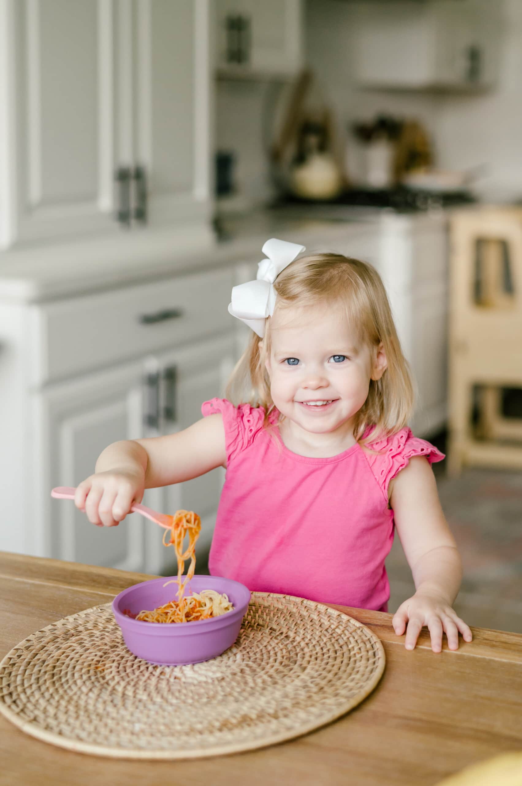 Young girl sitting at a table eating a bowl of spaghetti.