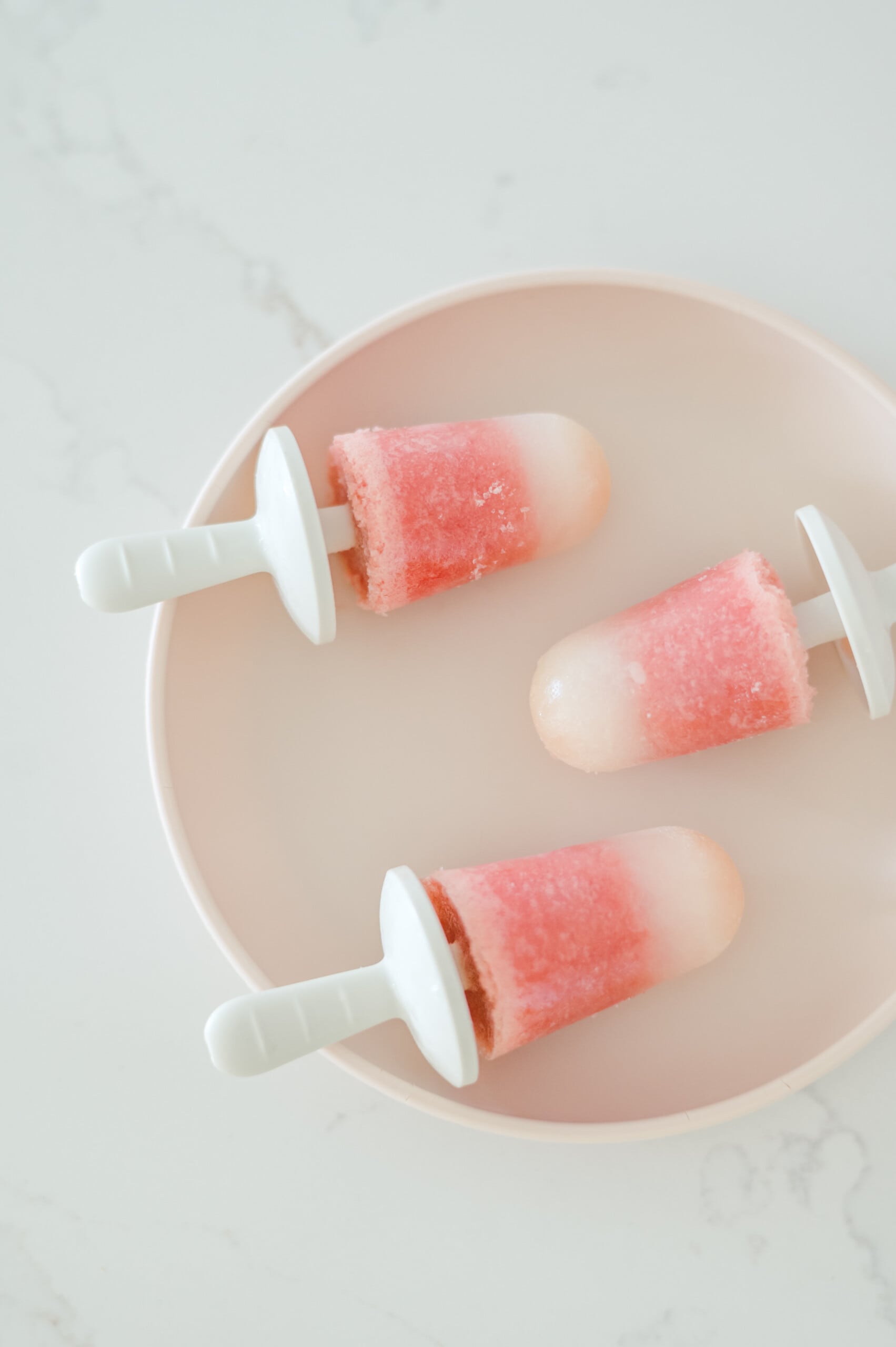 Plate of three small watermelon popsicles on top of a white kitchen counter.