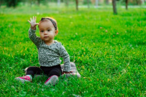 Happy baby waving hello sitting on green grass lawn