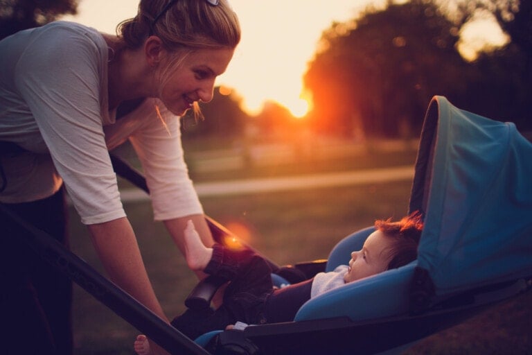 Mother leaning down and smiling at her baby who is sitting in his stroller looking up at her.