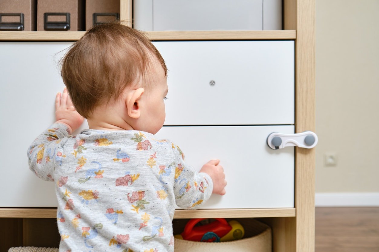 Toddler boy trying to open a cabinet door but there is a baby proofing lock on the cabinet prohibiting him from opening it.