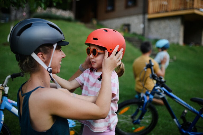 A young mother with little daughter preparing for bike ride, putting on helmets.