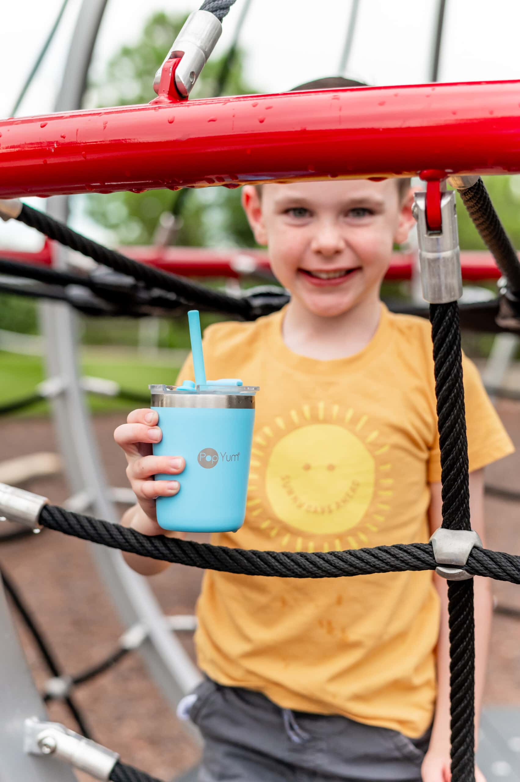 Young boy on the playground holding the blue PopYum Kids Cup