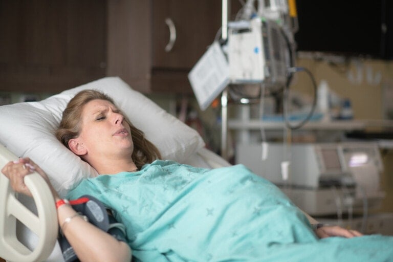A pregnant woman lies in her bed in the delivery room, griping the handrail while trying to breathe through labor and contraction pains