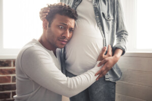 Handsome African American man is listening to his beautiful pregnant wife's tummy, feeling shocked