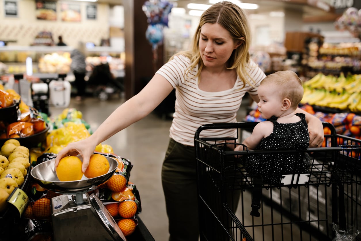 A mother with her little daughter buying fresh fruit at the grocery store