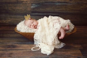 A beautiful, newborn baby girl wears a small golden crown. She is draped with lace and pearls ~ a princess!