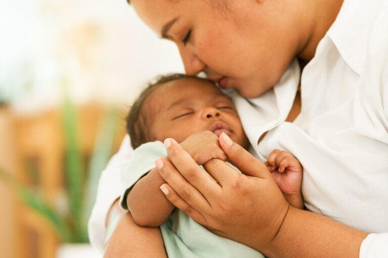 African Newborn baby one-month-old holding fingers mother's hand, sleep relax worry-free in warm embrace mom. image with a shallow depth of field, Select focus area hand. concept family mixed race.