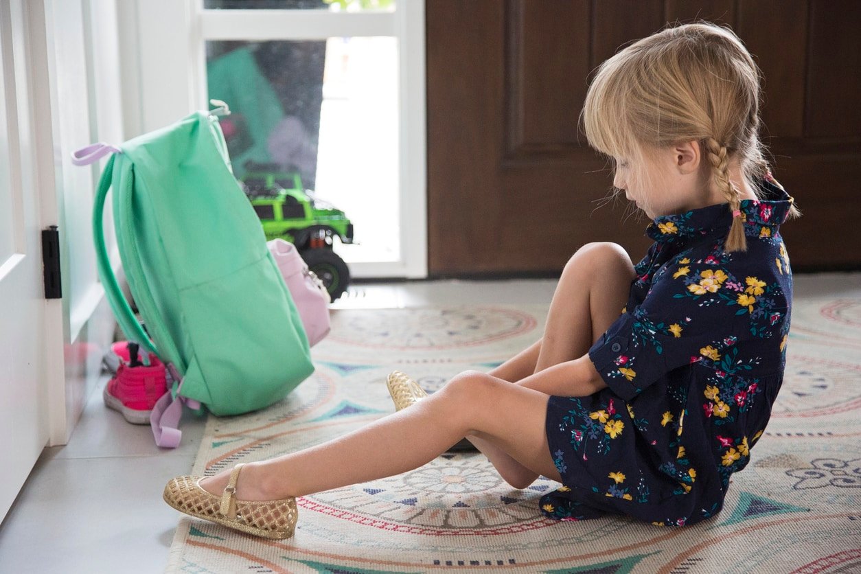Little girl puts on shoes while anxiously anticipating her first day of kindergarten