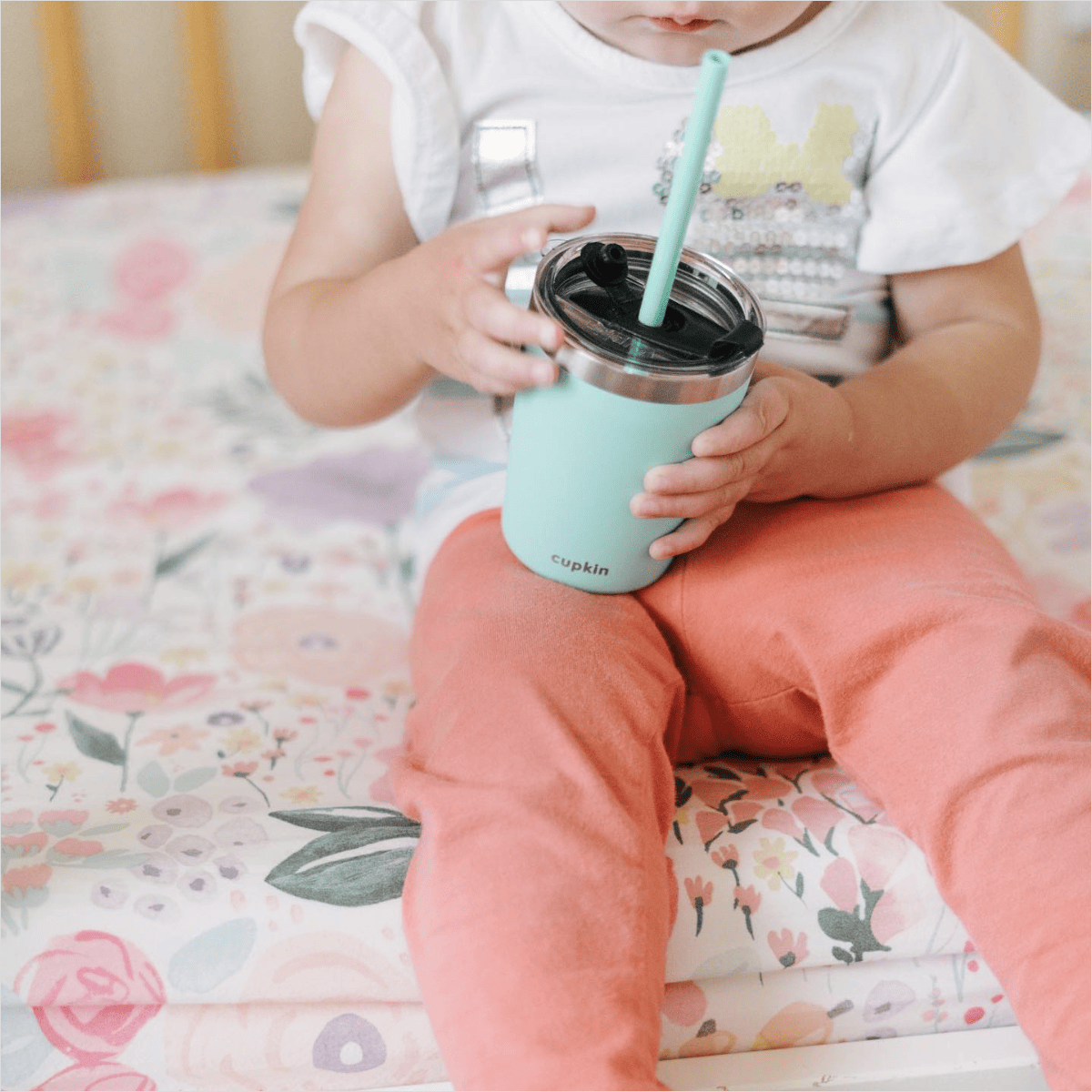 Little one sitting on bed drinking from a Cupkin cup