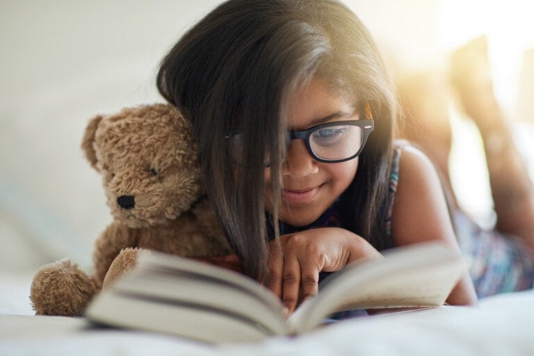 Shot of a cute little girl reading a book in her bedroom with her teddybear by her side
