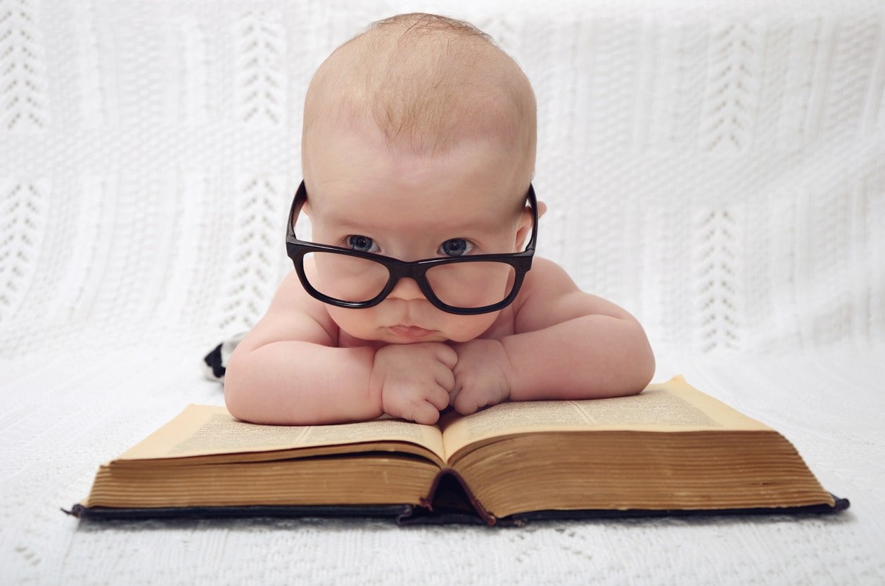funny portrait of cute baby in glasses lieing over an old big book (vintage style)