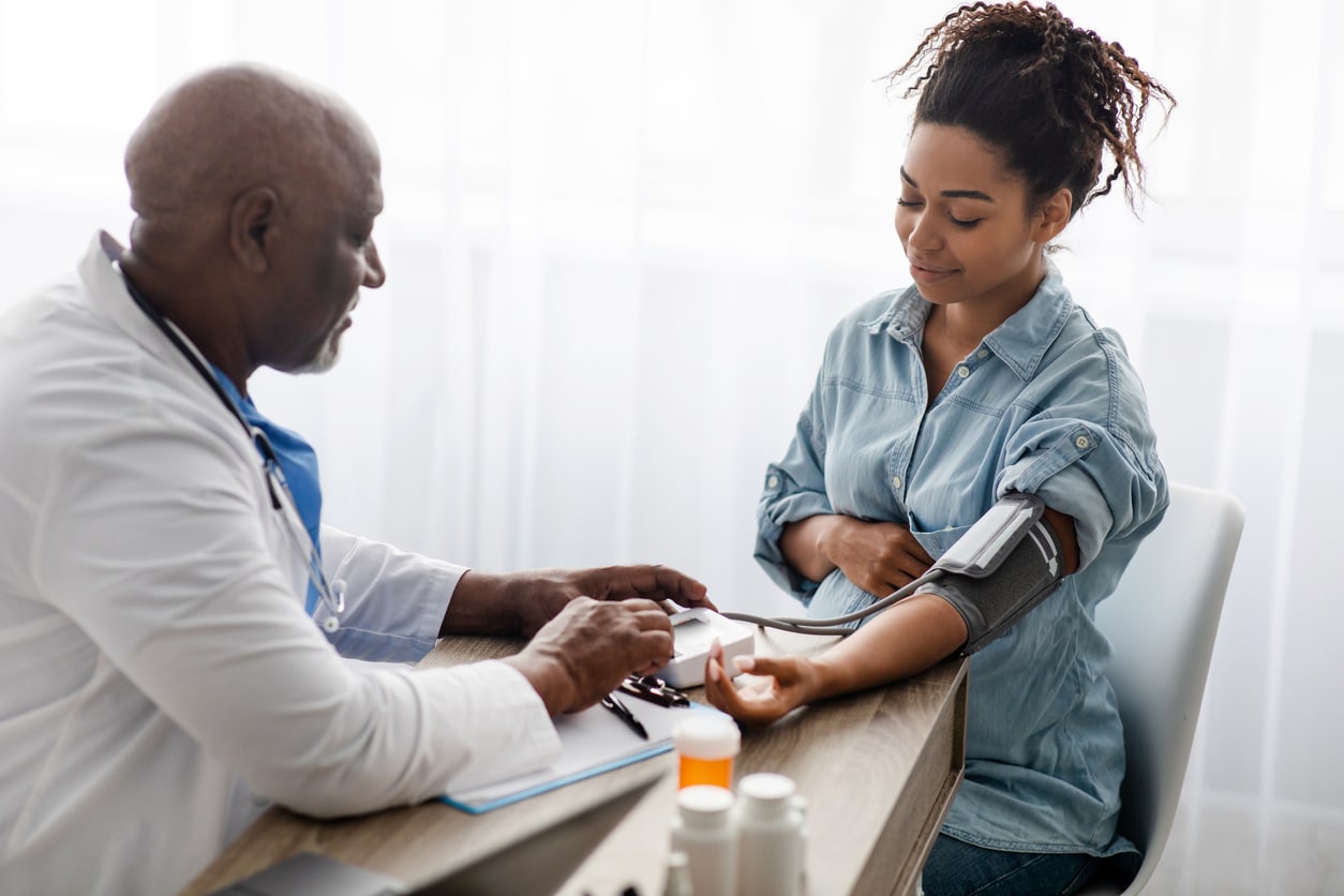 Gestational Hypertension. Mature Male Medical Worker Measuring Arterial Blood Pressure Of Pregnant Black Woman Using Cuff, Patient Having Problems With Tension, Sitting At Table. Health Care Concept