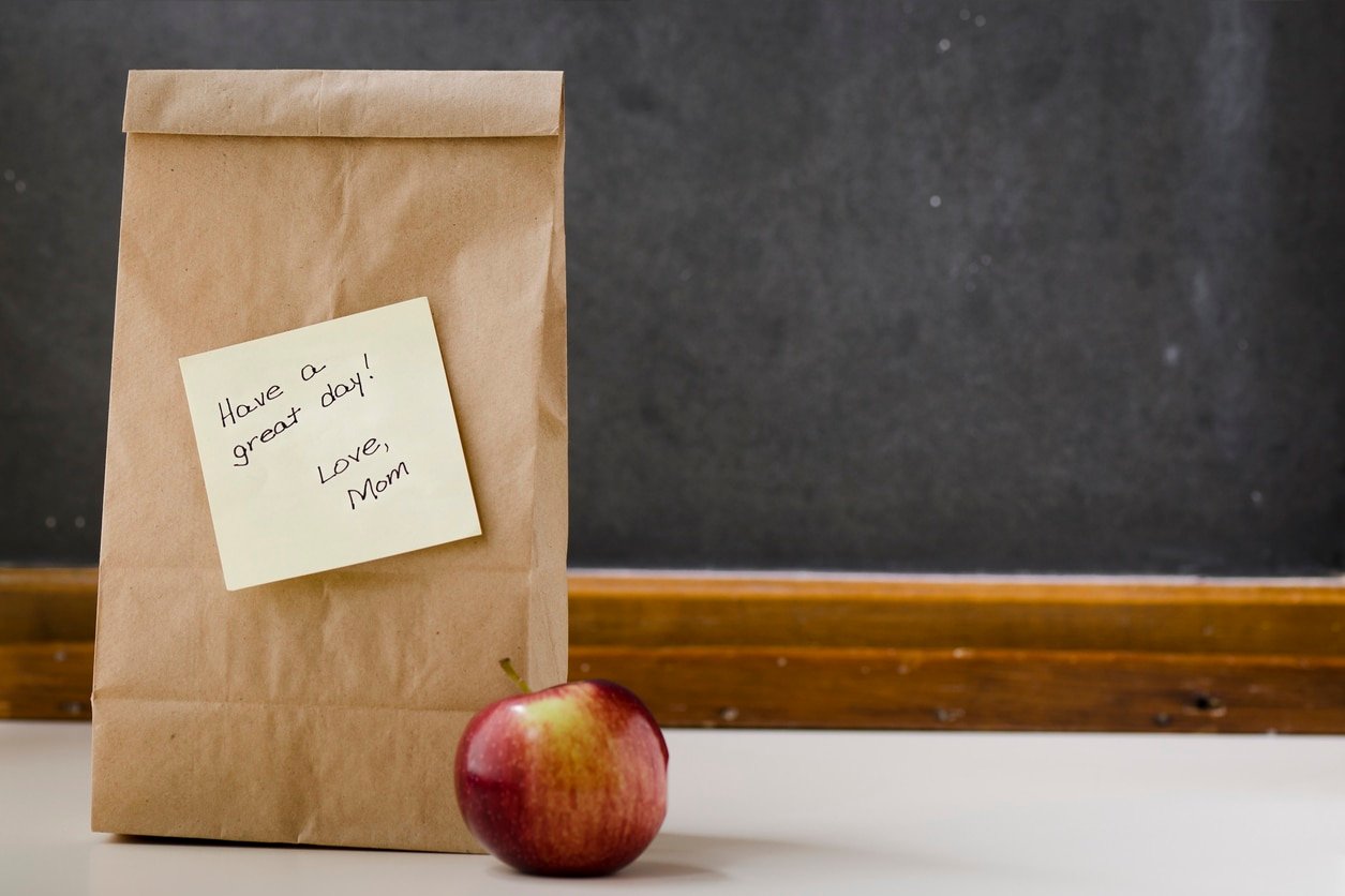 A paper lunch bag with a note from mom with an apple and a blackboard in the background with room for copy.