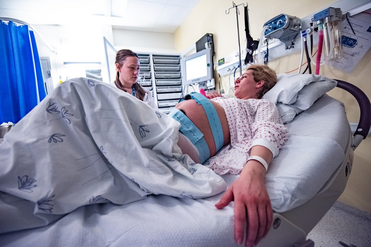 Pregnant woman lying down in a hospital bed and talking to a doctor.