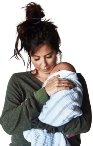 Shot of a young woman looking down and holding her little infant son in a baby blanket. They are at home during the day.