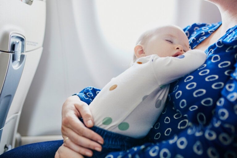 Woman with little girl travelling by plane. Mother holding her sleeping baby during the flight. Travelling with kids