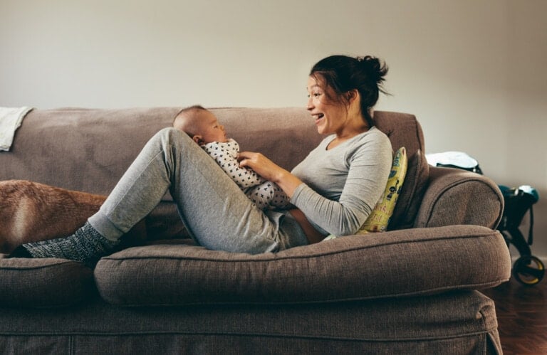 Woman lying on a couch pampering her baby. Smiling mother talking and playing with her infant baby.