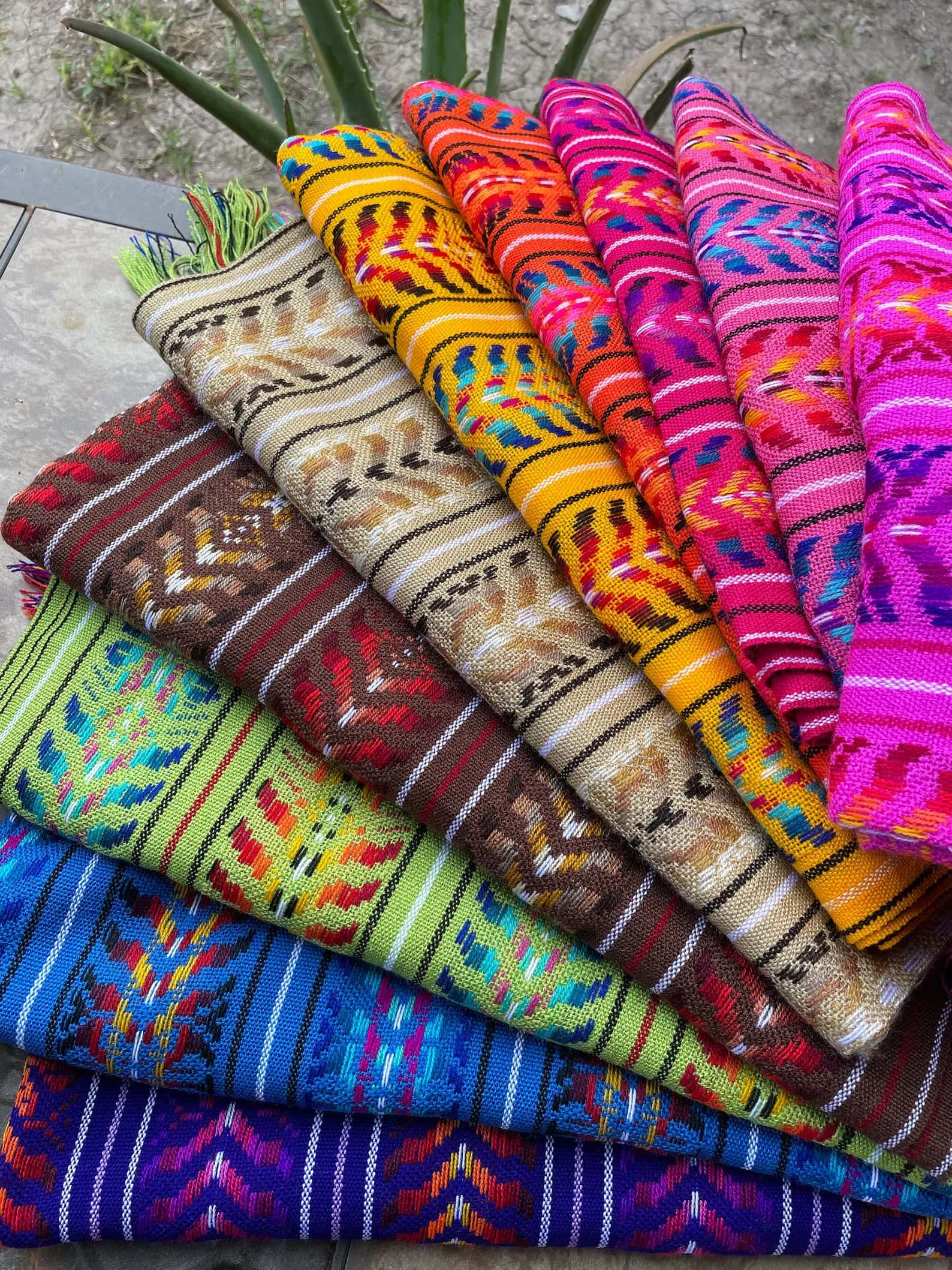 Different colored rebozos folded and spread across on the floor.