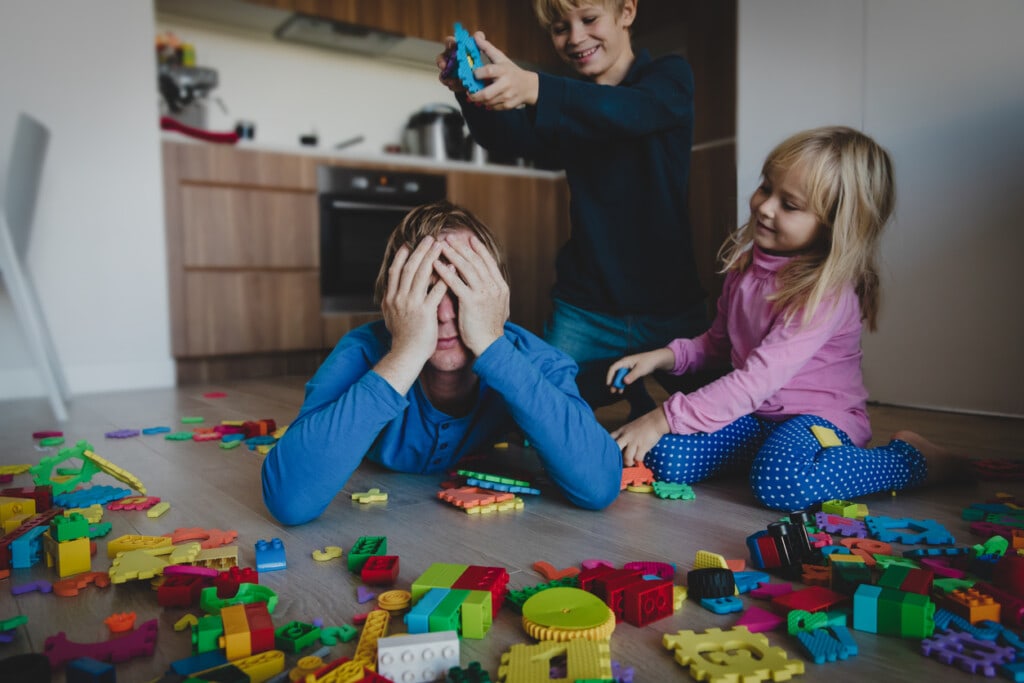 kis play with toys scattered all over and tired exhausted father, difficult parenting