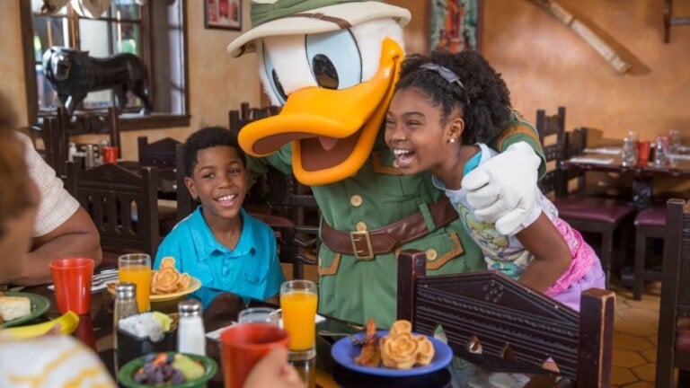 two children eating lunch and hugging daffy duck at disney world