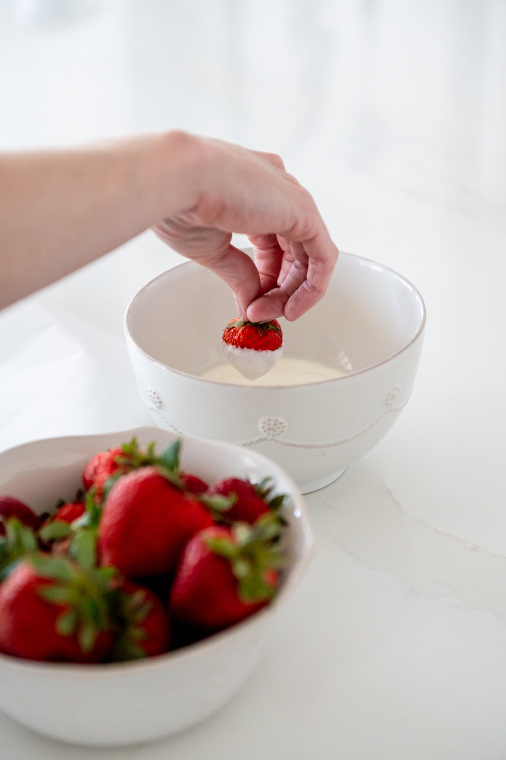 Hand dipping a strawberry into a white bowl of Stonyfield plain yogurt