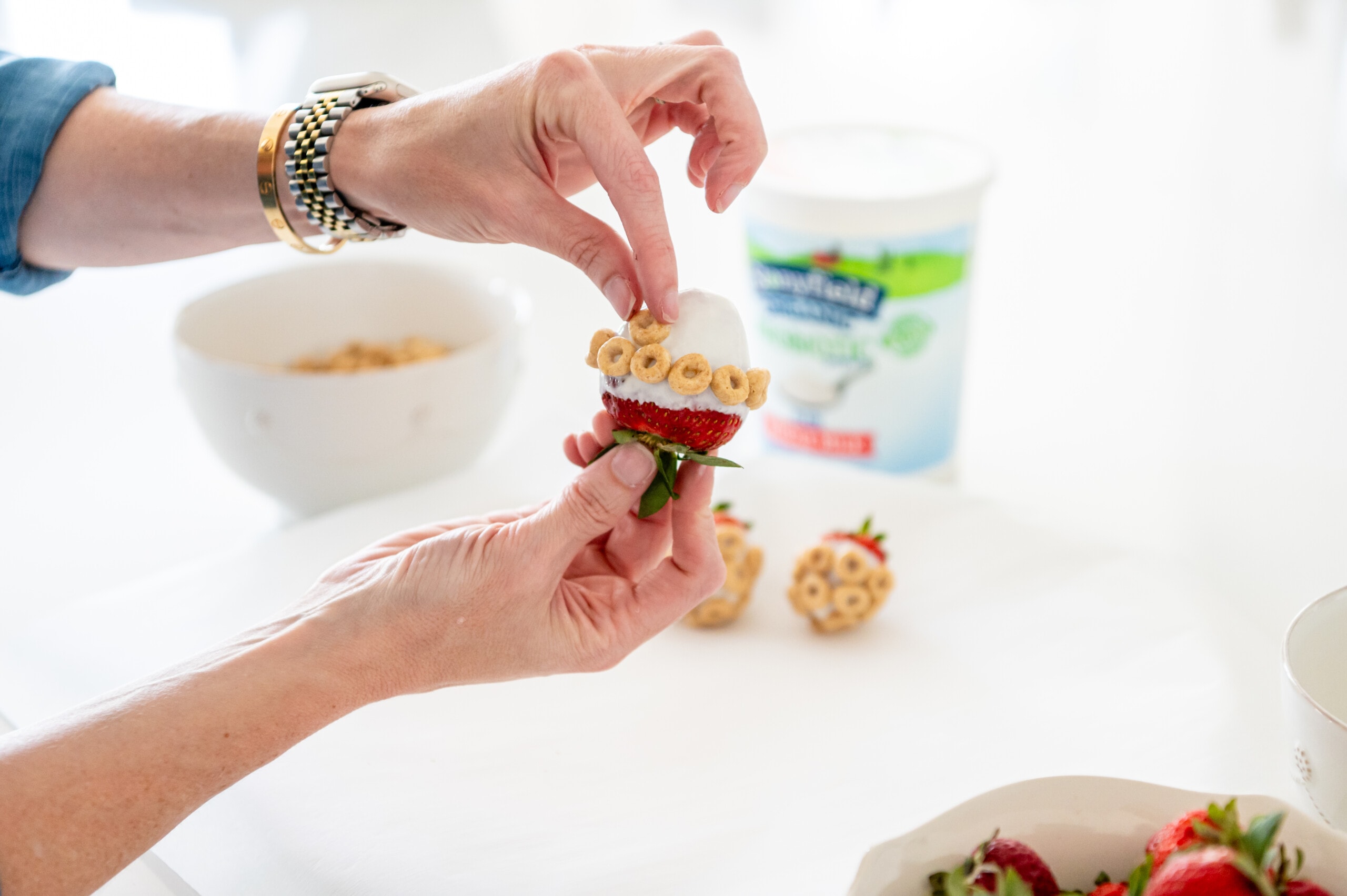 Hands carefully putting cheerios on the yogurt covered strawberry.